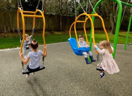 インクルーシブなブランコ（姿勢が補助され、向かい合って乗ることができる）に乗って遊んでいる子どもたち